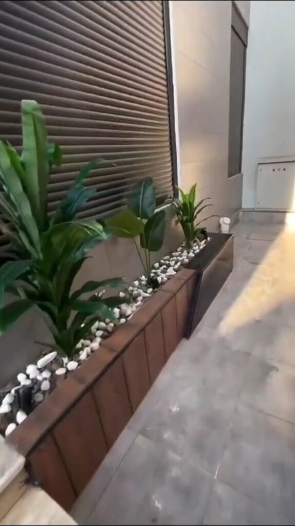 حوض زراعي مغلف بنباتات صناعية وحصى أبيض بجانب مدخل الفيلا